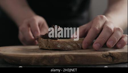 man spreading chocolate hazelnut spread on ciabatta slice on wood board, wide photo Stock Photo