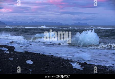 A blue iceberg  sparkling in the sunset on a black sand beach. Stock Photo