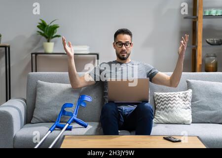 Injured Man With Broken Leg And Crutches Using Laptop Stock Photo