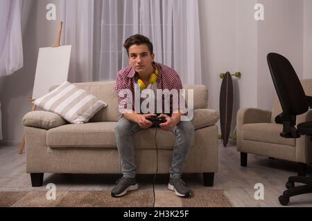 Teenage boy sitting on sofa playing computer games. Stock Photo