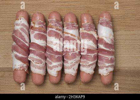 Preparation of raw sausages wrapped spirally in bacon on a wooden background. Top view. Stock Photo