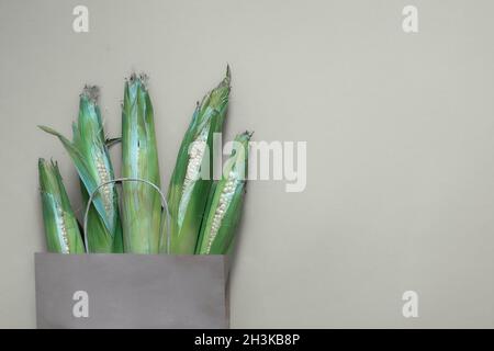 Paper craft bag with corn harvest on white background. Top view of different groceries farm shop, fresh vegan green food delivery. Stock Photo