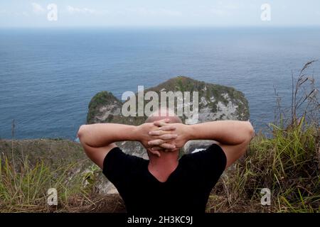 Man sitting on the cliff and admiring amazing view in Nusa Penida Stock Photo