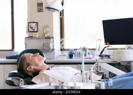 Middle aged woman on dentist stretcher with tools all over the room. Female patient waiting for checkup Stock Photo