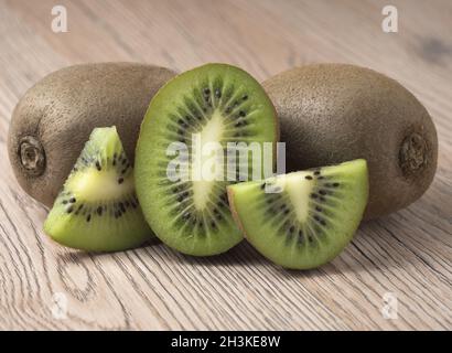 Ripe juicy kiwi fruit with sliced segments on wooden background. Stock Photo