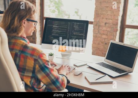 Back rear view photo of young man use laptop programmer coder jawascript linux developer sit desk indoors Stock Photo