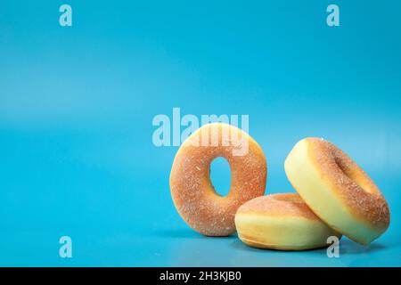Pile with three simple donuts with sugar isolated on blue background with copyspace, fast food,sugar concept Stock Photo