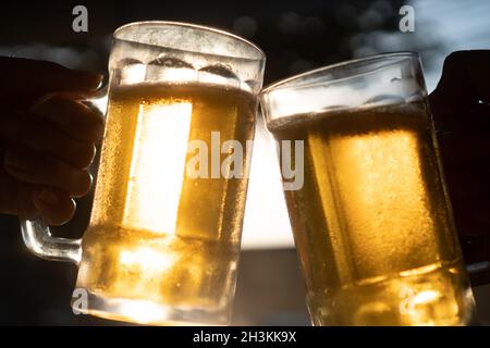 Closeup toast clinking fresh lager beer mugs with sun rays in hot summer day Stock Photo