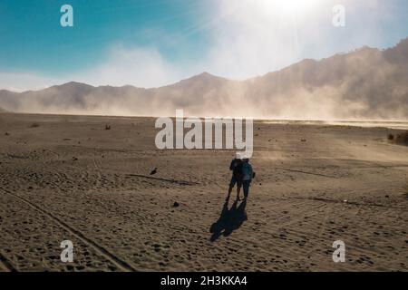 Cinematic shot aerial view of tourists walking in a volcanic dusty desert near beautiful Mount Bromo in East Java Stock Photo