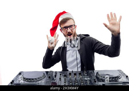 Funny emotional dj in Santa's hat, glasses plays music on a turntable raises hands up. studio shot  Stock Photo