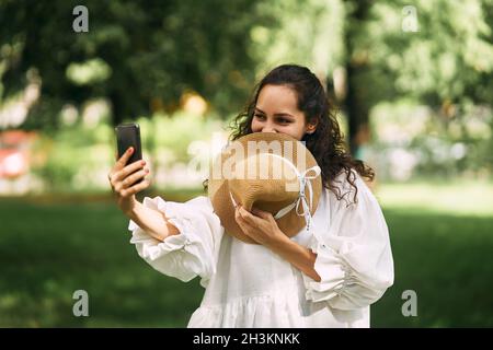 Young beautiful girl in a hat makes a selfie on her phone in the park Stock Photo