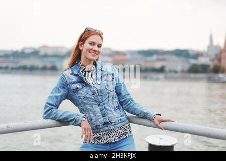 Happy young redhead Caucasian woman posing at riverbank Stock Photo