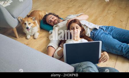 A Lovely Couple Lying on the Floor Using a Laptop, spouses enjoying of Each Other. Stock Photo