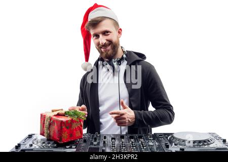 Funny dj guy in Santa's hat holds gift box while standing behind a turntable. New Year party Stock Photo