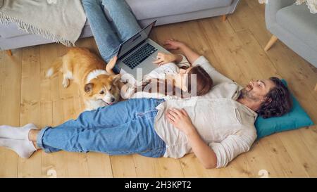 A Lovely Couple Lying on the Floor Using a Laptop, spouses enjoying of Each Other. Stock Photo