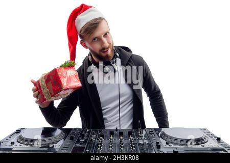 Funny dj guy in Santa's hat shaking gift box while stands behind a turntable. New Year party Stock Photo