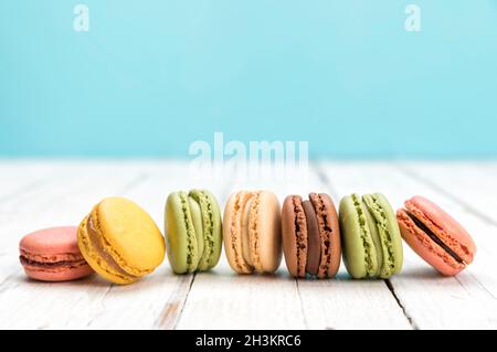 Row of colorful macarons on rustic white table. Delicious French pastry assortment closeup with copy space. Stock Photo
