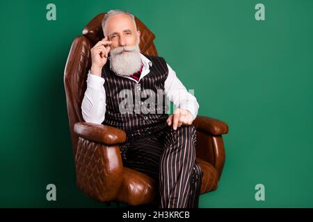 Photo of experienced bearded english aristocrat sit armchair relax wear striped suit on green color background Stock Photo