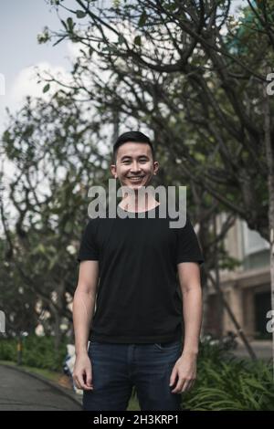Portrait of asian young handsome man in casual clothing standing on the street and smiling. Asia, Chinese people, real life concept, sunny day Stock Photo