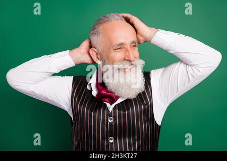 Photo of cheerful well-groomed man look empty space touch hair wear classy striped suit on green color background Stock Photo