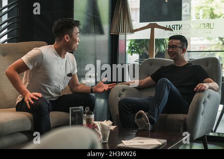 Two asian young men sitting in coffee shop, drinking coffee, talking enthusiastically. millennials life, lifestyle in the city Stock Photo