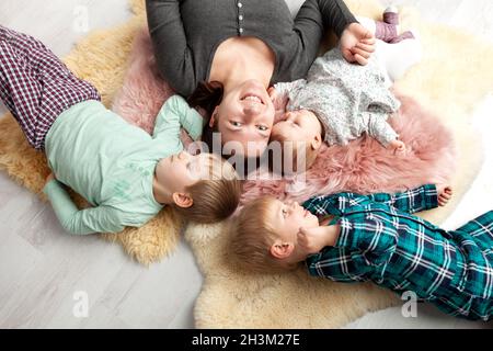 Top view of beautiful young mother, their cute little daughter and two son, lying on wooden floor. Stock Photo