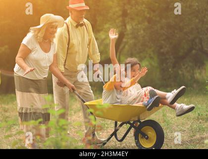 Grandma And Grandpa Are Riding Their Grandchildren In A Wheelbarrow Stock Photo
