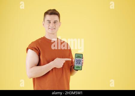 Serious young man in medical mask pointing at smartphone with covid-19 vaccine passport Stock Photo