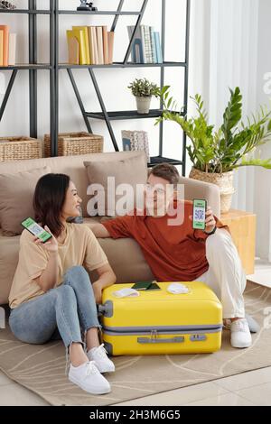 Young couple sitting on the floor at home next to suitcase happy after getting negative covid-19 test results Stock Photo