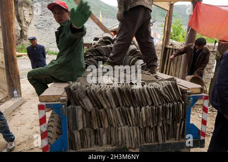Builders / roofers dismantling an old building 's roof and carefully removing old vintage tiles for recycling. Songpan in northern Sichuan, China. The tiles could be part of a reclamation project and destined for reuse elsewhere or even return to an overhauled roof on the same building. (125) Stock Photo