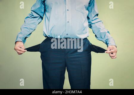 businessman standing on the green background and showing his empty pocket, turning his pocket inside out, no money concept