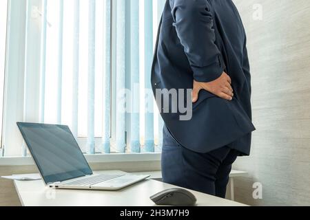 Man in desk office suffering from back pain. office worker holds his hand over his sore back. Health problems from sedentary work. Stock Photo