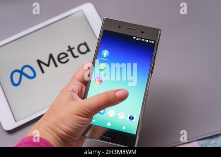 Smartphone display with logo of Facebook, WhatsApp and Instagram apps in hand in against blurred META logotype on white background tablet monitor: Tal Stock Photo