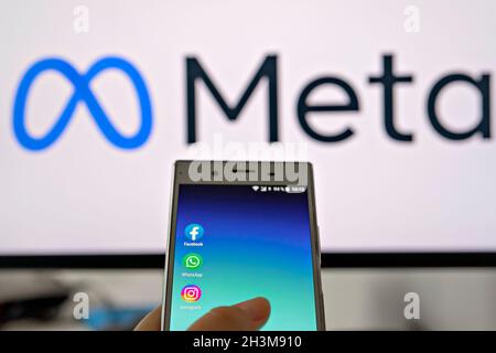 Smartphone display with logo of Facebook, WhatsApp and Instagram apps in hand against blurred META logotype on white monitor background: Tallinn, Esto Stock Photo