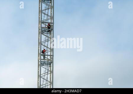 Two tower crane operators climb down the ladders high in the sky at the end of a working day on a construction site. Stock Photo