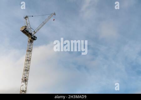 A low angle view of a tall tower construction crane set against the blue sky background late on a sunny afternoon. Stock Photo
