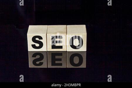 SEO text on wooden cubes on black glass background. Stock Photo