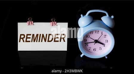 Reminder, text on sticker. There is an alarm clock on a black background Stock Photo