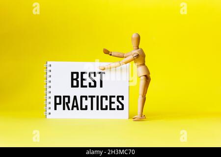 Best practices, the text is written on a notebook, next to a wooden doll on a yellow background. Positive quote. Stock Photo