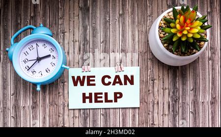 We can help text on a sticker, a flower in a pot and an alarm clock on a wooden table. Stock Photo