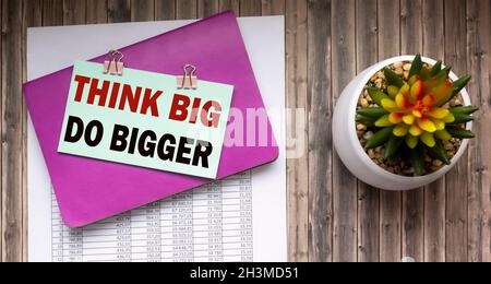 Think big, do bigger motivational quote written on note paper. Notepad, papers and cactus on a wooden table Stock Photo