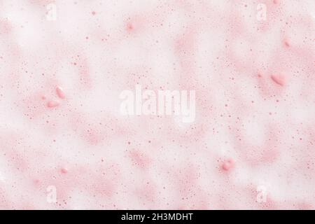 Texture soapy foam of cosmetic cleanser on pink surface. Beauty product bubble pattern. Stock Photo