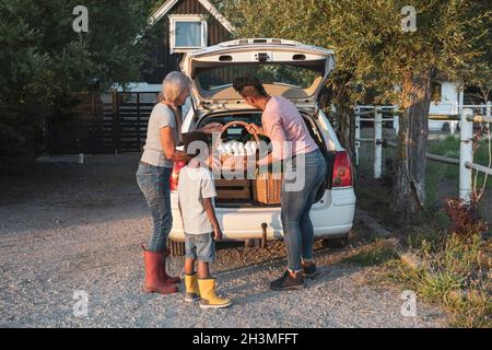 Boy standing by mother and grandmother keeping eggs basket in car trunk Stock Photo