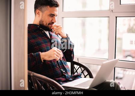 Happy thoughtful man using laptop computer at home Stock Photo