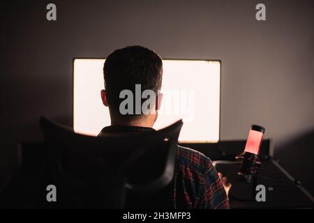 Rear view of man sitting at desk working on computer Stock Photo