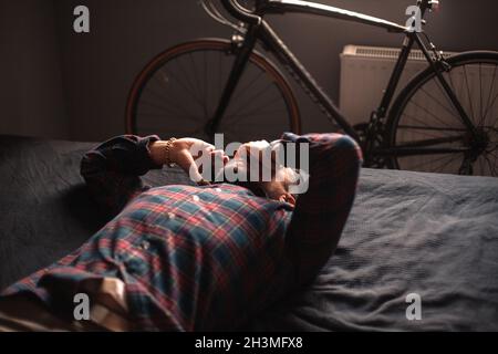 Exhausted man talking on smart phone lying on bed at home Stock Photo