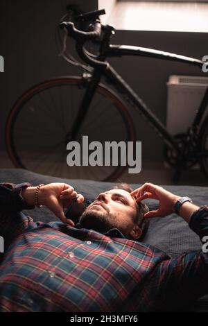 Thoughtful man talking on smart phone lying on bed at home Stock Photo