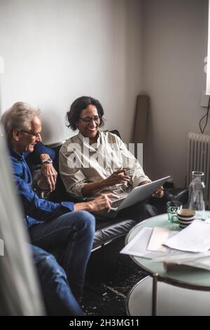 Smiling male and female colleagues discussing over laptop in office Stock Photo