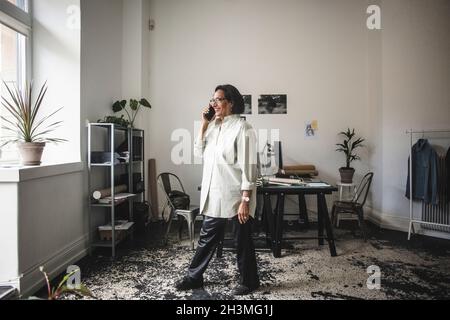 Smiling female owner talking on smart phone at workshop Stock Photo