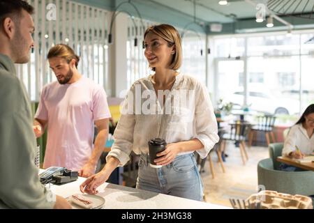 Female client with coffee to go smiling and taking dessert from barista in cafe Stock Photo